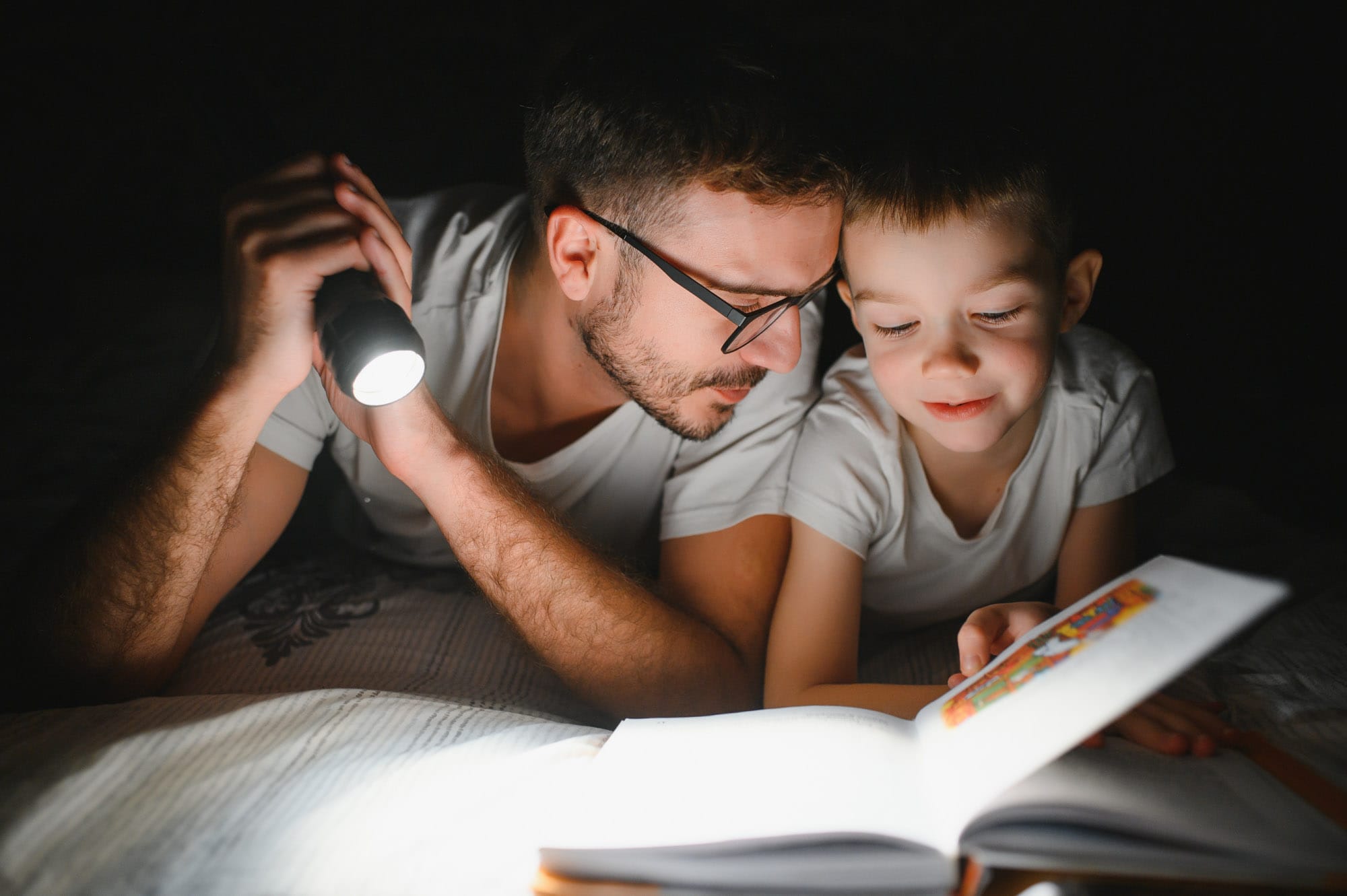 Father and son reading with flashlight