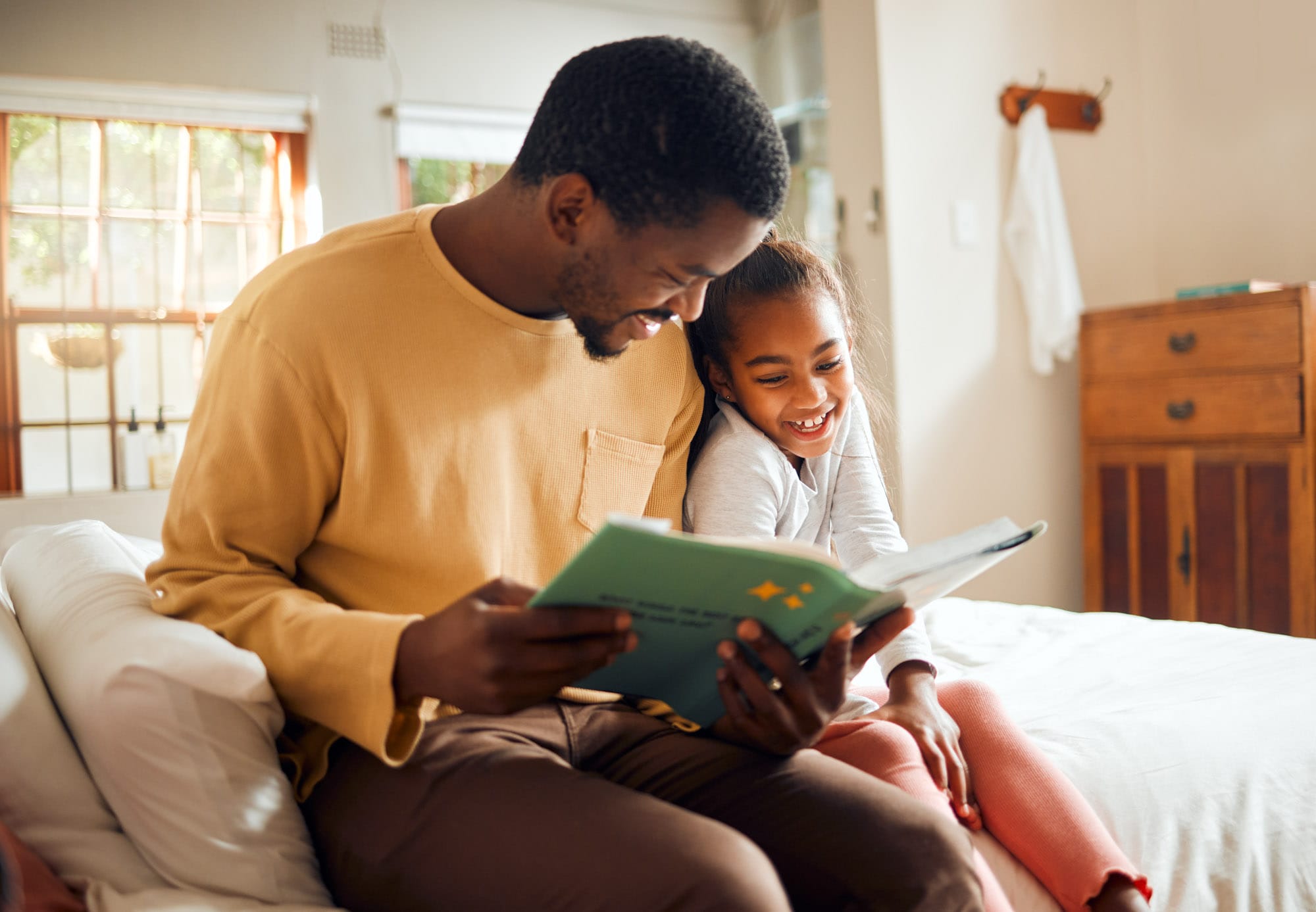 Father reading storybook with daughter on bed.